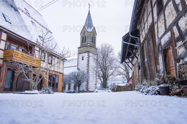 A snowy church tower next to half-timbered houses in a quiet village, Gechingen, Calw district, Germany
