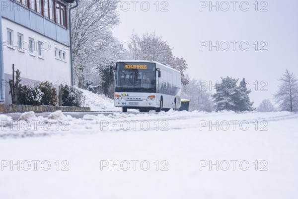 A bus travels on a snowy road surrounded by trees and buildings, Gechingen, Calw district, Germany