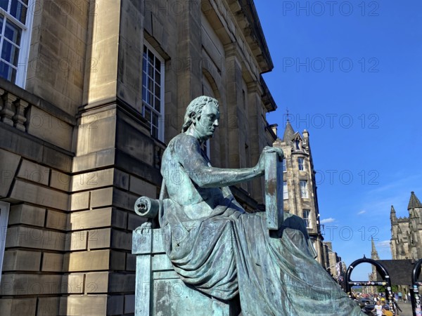Bronze statue of a man sitting in front of a historic building under a clear sky