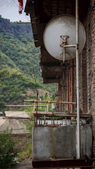 Old satellite dish on the balcony of a building with views of green mountains, Armenia