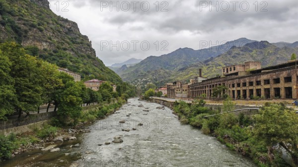 A river flows through a valley surrounded by mountains and old factory buildings, Armenia