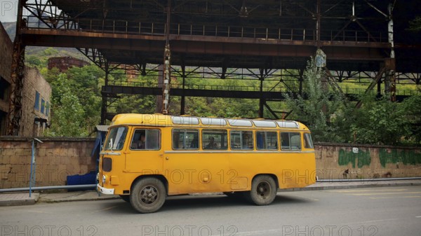 An old Nostaligian yellow bus in front of an abandoned factory, Armenia