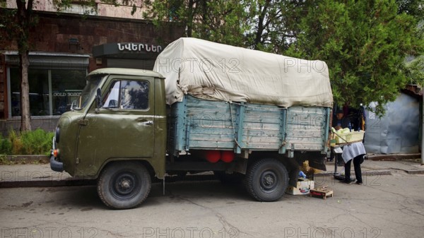 A vintage truck with a tarp on a road surrounded by trees, Armenia