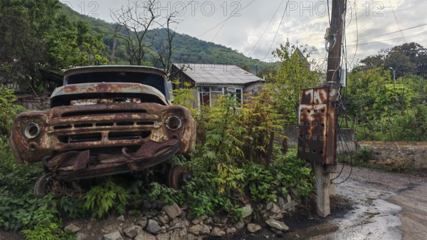 An old, rusty truck stands in front of a power pole in a green setting, romantic, rural atmosphere, Armenia