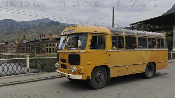 A yellow retro bus drives through an industrial area in a mountainous landscape, Armenia