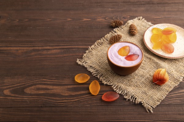 Purple Yogurt, with jelly candy on brown wooden background and linen textile, side view, copy space, minimalism