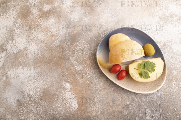 Smoked Mozzarella cheese, with tomatoes and olives on brown concrete background, top view, flat lay, copy space