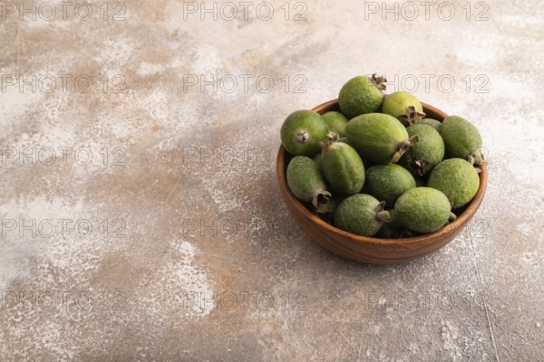 Ripe Feijoa in wooden bowl on brown concrete background, side view, copy space, minimalism