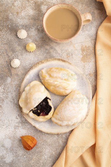 Glazed Pies with blueberry jam on brown concrete background and orange linen textile, cup of coffee, top view, flat lay, close up