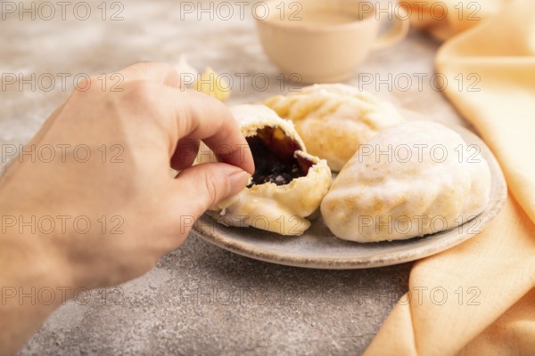 Glazed Pies with blueberry jam on brown concrete background and orange linen textile with hand, cup of coffee, side view, close up, selective focus