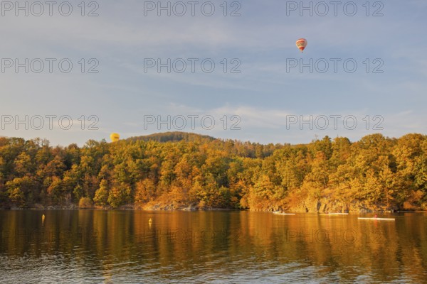 Hot air balloons over the Brno Reservoir (Brnenská prehrada) on the Svratka River on a sunny autumn day. Four rowing boats and a motorboat can be seen. The reservoir is located northwest of the city of Brno in the Czech Republic