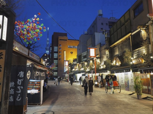 Bustling street scene in the evening with illuminated shops and passers-by, Nishi-Asakusa, Tokyo, Japan