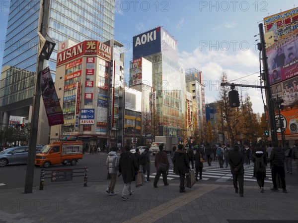 People cross a busy city street surrounded by modern buildings and commercials, Akihabara Electric Town, Tokyo, Japan