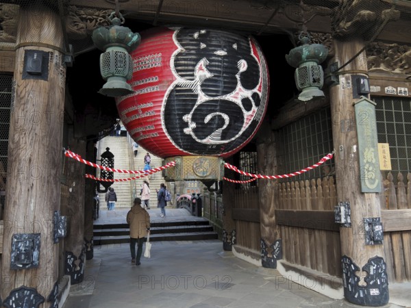 A large temple with an impressive lantern and traditional wooden construction, people enter the site. Niomon Gate, Narita, Japón