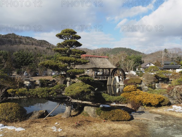 Japanese garden with traditional house and well-kept trees against mountain backdrop, Oshino Hakkai, Kawaguchiko, Japan