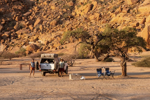 Camping in the Spitzkoppe desert under a tree next to a vehicle, surrounded by impressive rock formations, Spitzkoppe, Namibia