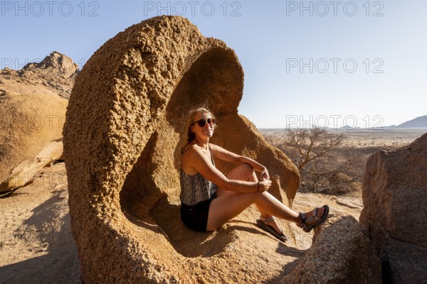 Woman sitting quietly in a rock in the sunny desert landscape, Spitzkoppe, Namibia