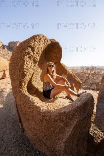 Young woman sitting relaxing in a rock cave in sunny weather, Spitzkoppe, Namibia