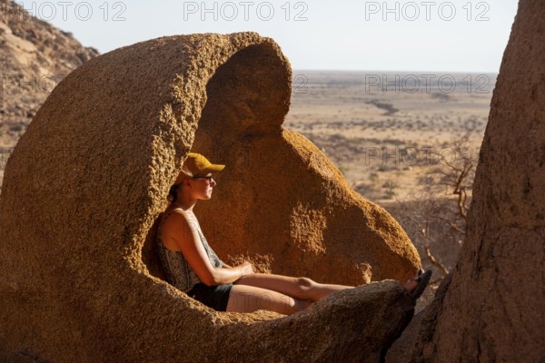 Person sitting relaxing in a natural rock area and enjoying the view of the desert, Spitzkoppe, Namibia