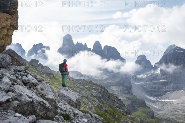 Female mountaineer looking at fog and Torre Di Brentai, rocky mountain peaks and mountain landscape, Brenta Mountains, Brenta-Adamello Natural Park, Trentino, Italy