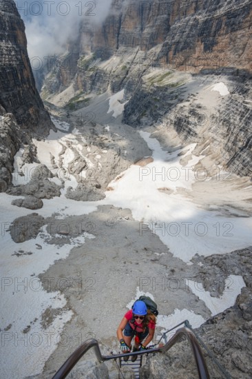 Mountaineers climb a ladder on the Via Ferrata Oliva Detassis via ferrata, rocky mountain peaks and mountain landscape, Brenta Mountains, Parco Naturale Brenta-Adamello, Trentino, Italy