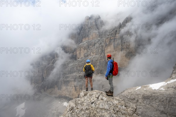 Climbers on the Via Ferrata Oliva Detassis via ferrata in fog, rocky mountain peaks and mountain landscape, Brenta Mountains, Parco Naturale Brenta-Adamello, Trentino, Italy