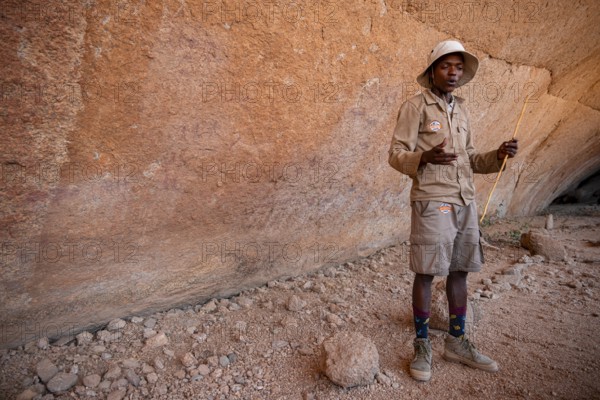 Bushman's paradise, guide standing in front of a massive red rock wall in a desert-like environment, Spitzkoppe, Namibia