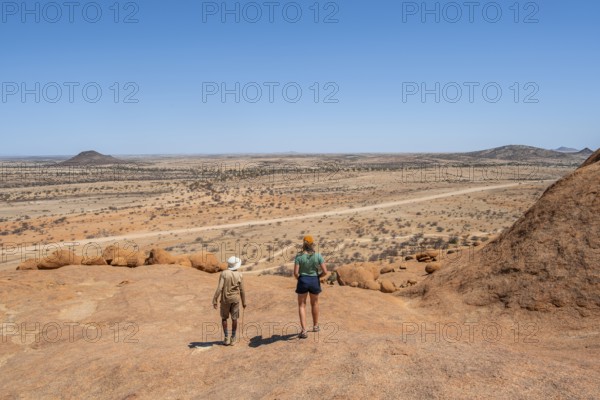 Bushman's paradise, tourist and guide hiking through the vast, dry desert landscape, Spitzkoppe, Namibia