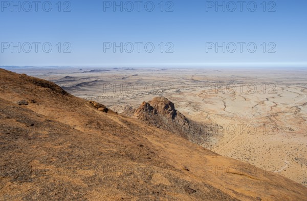 View from a hill over the endless dry desert landscape under blue sky, Spitzkoppe, Namibia
