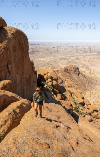 Young woman hiking on rocky hill under blue sky in dry landscape, Spitzkoppe, Namibia