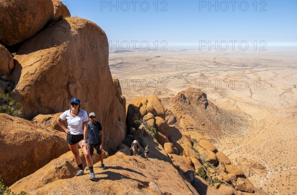 Tourists hiking on a rock with a view of a vast desert landscape, Spitzkoppe, Namibia
