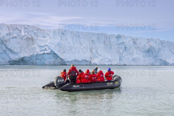 Eco-tourists in Zodiac boat from Poseidon Expeditions looking at Brasvellbreen glacier wall debouching into the Barents Sea, Svalbard / Spitsbergen