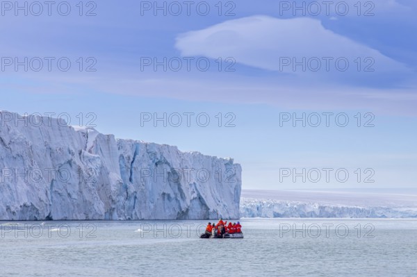 Eco-tourists in Zodiac boat and Brasvellbreen glacier wall from ice cap Austfonna debouching into Barents Sea, Nordaustlandet, Svalbard / Spitsbergen