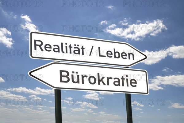 (photo montage) Directional arrows against a blue sky with the inscription REALITY/LIFE and BUREAUCRACY