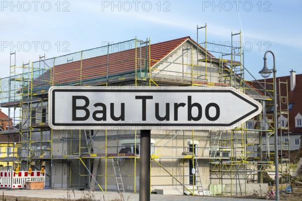 (Photo montage) Direction arrow with the inscription BAUTURBO in front of the construction site of a new residential building