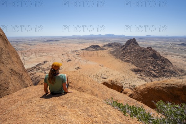 Woman sitting on rocks and enjoying the view over the barren desert landscape of Spitzkoppe, Spitzkoppe, Erongo, Namibia