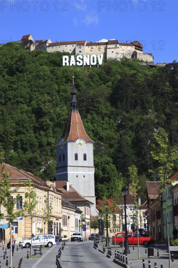Town of Rasnov, German Rosenau. In the foreground is the distinctive clock tower of the Protestant Church, St. Matthias Church, in the background on the hill is the medieval Rasnov Fortress, Rosenau Castle, Brasov District, Transylvania, Romania