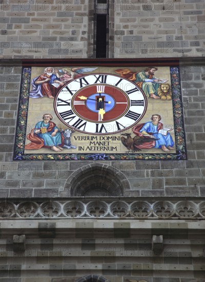 The picture shows the striking tower clock of the Black Church, Biserica Neagr, in Brasov, Brasov, Romania. The city's landmark is home to an ornate clock face that combines both religious symbols and a Latin inscription. Characterised by the four evangelists, the clock face is surrounded by the four canonical evangelists, each depicted with their traditional symbols: Matthew (man/angel), Mark (lion), Luke (bull) and John (eagle)