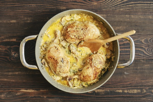 Top view of homemade creamy chicken thighs with mushroom sauce in skillet, served with herbs on rustic wooden surface