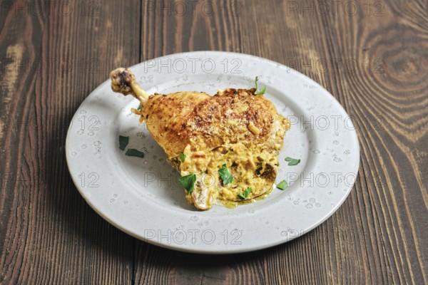 A chicken leg cooked and placed on a round plate. The dish features a creamy mushroom sauce and is garnished with green herbs