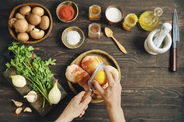 Top view of hans grating lemon zest over raw chicken. Person marinates chicken with dry aromatic spices. High angle view of culinary process