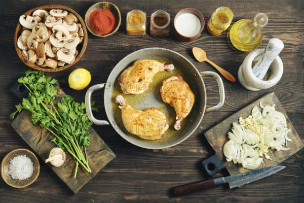 Top view of chicken poultry browning in oil. Culinary process of making dinner with sliced mushroom, onion, and garlic on a dark rustic background
