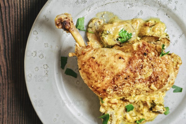 Close-up top view of roasted chicken leg on a round plate with a creamy mushroom sauce and herbs