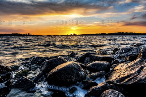 A colorful sunset over Lake Vänern with waves hitting dark rocks, Värmlands Näs, Värmlands län, Sweden