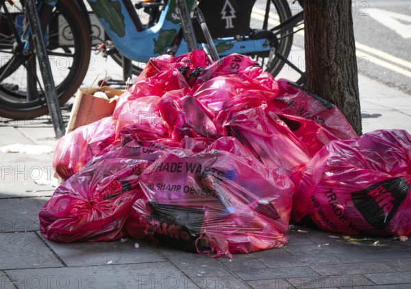 A pile of pink plastic bags with the words Trade Waste lying on the side of the road on the sidewalk, London, England, Great Britain