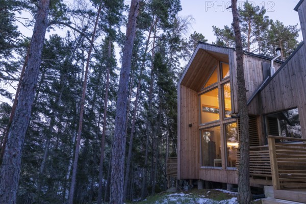 Modern wooden house in the forest, illuminated from within and inviting at dusk, Korpoström, Korpo or Korppo, southwestern archipelago, Finland