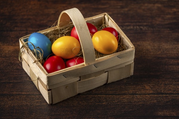 Colourful easter eggs in a small wooden basket on a rustic wooden surface