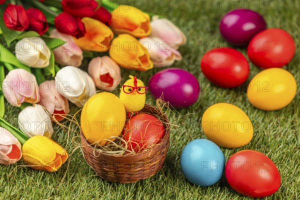 Colourful Easter eggs and a chick figure in a nest next to colorful tulips