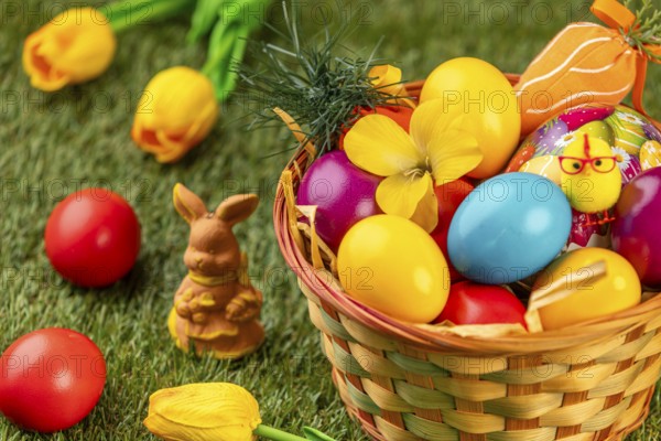 Colourful Easter eggs in a basket with a rabbit figure and flowers on grass