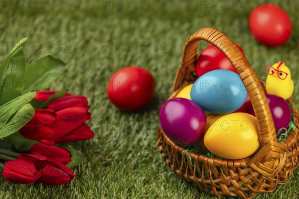 A basket of colorful Easter eggs next to flowers in a meadow